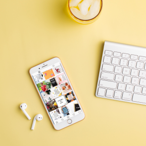 iPhone open to Instagram next to a white keyboard on a yellow surface; earbuds on the left side