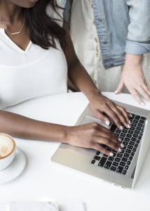 profiles of 2 women standing by a keyboard. One is typing.