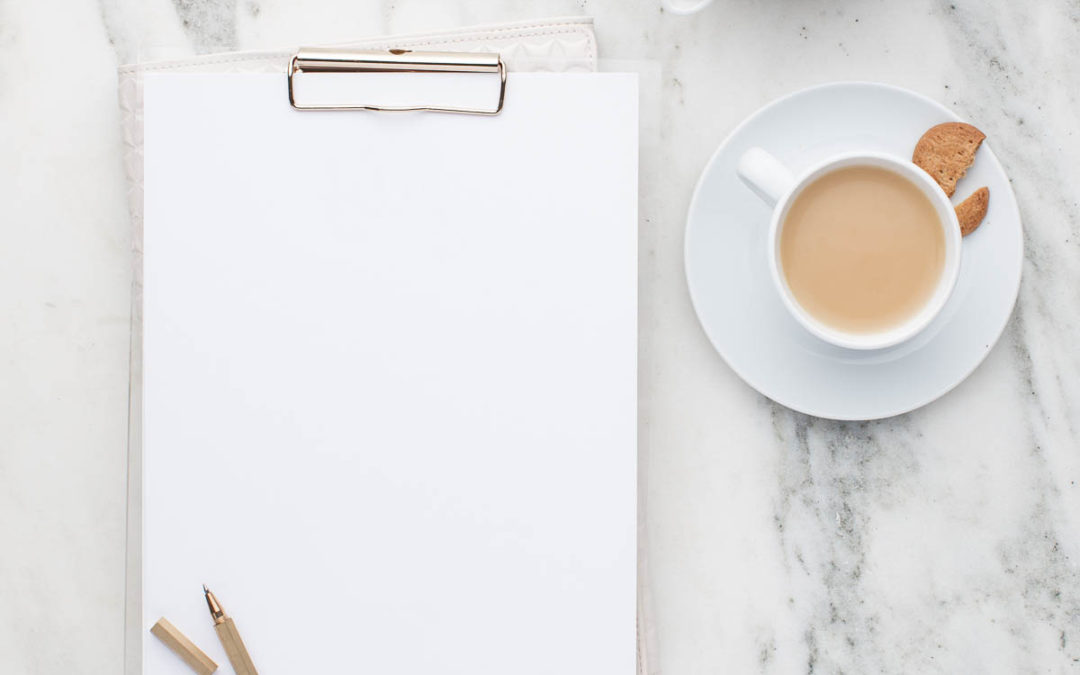 Flat lay of a blank notepad with a pencil on it. There is a cup of coffee and a small coffee pot beside it.