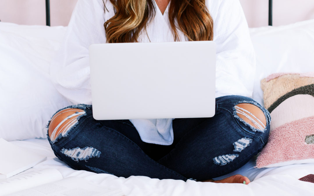 Young woman sitting on her bed with her laptop open on her lap